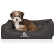 Kleiner flauschiger braun-weißer Welpe sitzt in einem dunkelbraunen Hundebett mit 'KNUFFELWUFF'-Logo.