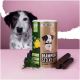 Ein Behälter mit "Darmwohl Sticks" mit Pfotenabdrücken steht auf einer pinken Oberfläche, umgeben von dunklen Leckereien und grünen Kräutern.