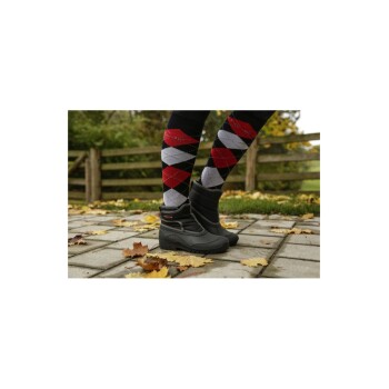 Die Beine einer Person, die schwarze wasserdichte Stiefel und bunte argyle-musterte Socken trägt, stehen auf einem mit Herbstblättern bedeckten Steinweg.