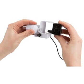 Eine Person hält ein Teil eines Haustier-Wasserbrunnens, verbindet eine schwarze Pumpe mit einer weißen Basis und einem Stromkabel.