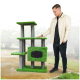 Ein Mann steht neben einem hohen, grünen Katzenbaum aus Kunstgras und grauen Pfosten, der mehrere Plattformen und einen gemütlichen Rückzugsort bietet.