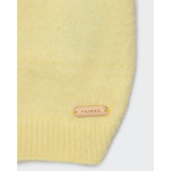 Nahaufnahme eines hellgelben gestrickten Haustierpullovers mit geripptem Saum und goldener Metallplakette mit der Prägung PAIKKA.