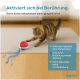 Katze spielt mit einem roten und transparenten interaktiven Spielzeug auf einem Teppich, deutscher Text beschreibt berührungsaktivierte Spielmerkmale.