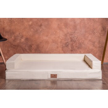 Ein cremefarbenes Haustierbett mit erhöhten Seiten, mit einem Lederetikett, das "tierland.de" liest, vor einem strukturierten braunen Hintergrund.