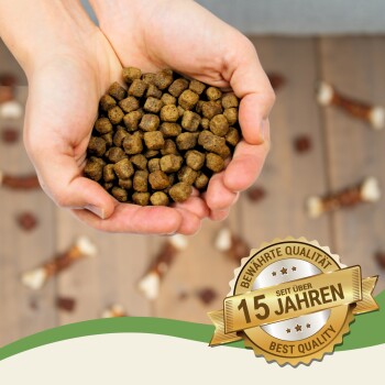 Hände halten einen Haufen brauner Haustierfutter-Kibble, mit einem Abzeichen, das 'Bewährte Qualität seit über 15 Jahren' und 'Beste Qualität' angibt.