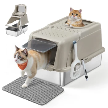 Eine beige Top-Entry Katzenstreu-Box mit einer grauen Matte, eine weiße Katze mit einem orangefarbenen Halstuch verlässt sie, und eine zweite Katze ist drinnen. Eine Schaufel ist befestigt.