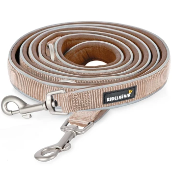 Eine aufgerollte beige Hundeleine mit einem silbernen Clip und einem schwarzen Etikett mit der Aufschrift 'RUDELKÖNIG.'