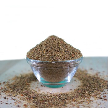 Eine klare Glas-Schüssel gefüllt mit einem Haufen Haustierkräuterergänzungsmittel, umgeben von verstreuten Kräutern auf einer hellen Oberfläche.