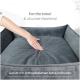 Eine Person drückt auf ein weiches graues Haustierbett mit strukturiertem Kissen und Etiketten "Komfortabel & druckentlastend" und "Gefüllt mit orthopädischen Schaumflocken."
