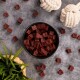 Eine schwarze Schüssel, gefüllt mit kleinen, quadratischen Stücken dunkler roter Haustierleckerlis, umgeben von verstreuten Stücken, einer grünen Pflanze und zwei weißen Seilspielzeugen.