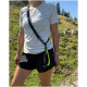 Person im Freien trägt eine über die Schulter getragene freihändige Hundeleine mit neongrünem Griff, weißem T-Shirt und schwarzen Puma-Shorts (Puma-Logo).