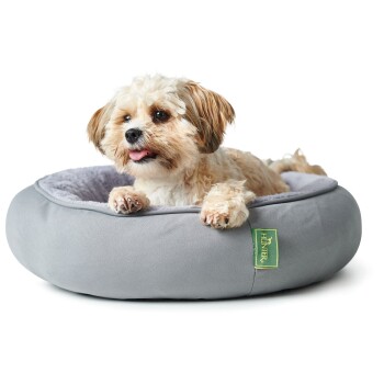 Ein kleiner Hund ruht auf einem weichen, runden grauen Haustierbett mit einem plüschigen Innenfutter. Das Bett hat ein grünes "Hunter"-Etikett.
