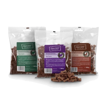 Drei transparente Beutel Chewies Trainingsknochen (Pansen, Rind, Geflügel) à 200 g mit verstreuten knochenförmigen Leckerlis davor.