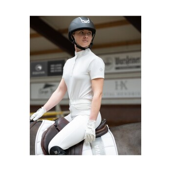 Ein Reiter in einem weißen Reitoutfit und Handschuhen sitzt auf einem Pferd, trägt einen schwarzen Helm. Der Hintergrund zeigt Reitsportbeschilderung.