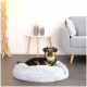 Ein schwarz-brauner Hund ruht auf einem flauschigen grauen Haustierbett in einem modernen Wohnzimmer mit einem hellgrauen Sofa und dekorativen Vasen auf einem weißen Tisch.