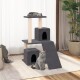 Eine graue Katze sitzt neben einem mehrstöckigen Kratzbaum mit zwei Verstecken und einer oberen Plattform, während eine andere Katze oben schläft.