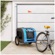Ein blauer und grauer Haustieranhänger mit einer kleinen orangefarbenen Fahne, geparkt neben einem Fahrrad auf einem Steinweg, mit Grün im Hintergrund.