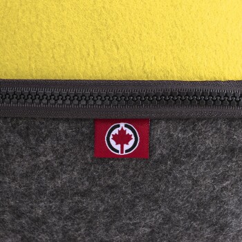 Nahaufnahme eines Haustierbettes mit einer gelben Oberseite und einem grauen Filzboden, mit einem Reißverschluss und einem roten Etikett mit einem Ahornblattlogo.