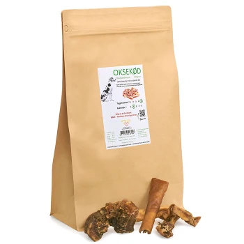 Braune Papiertüte mit Hundeleckerlis, beschriftet mit "OKSEKØD", mit einem weißen und grünen Nährwertaufkleber, umgeben von verschiedenen Hundekauartikeln.