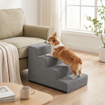 Braun-weißer Corgi klettert eine graue Haustiertreppe mit drei Stufen neben einem beigen Sofa in einem hellen Wohnzimmer.