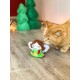 Eine verspielte orange Katze schnüffelt an einem bunten Plüschspielzeug, das einer Fee ähnelt, vor einem Hintergrund aus grünen Weihnachtsbäumen und sanften Lichtern.