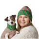 Ein kleiner Hund, der einen grün-braun gestreiften Pullover und ein passendes Halsband trägt, wird von einer Person in einem gemütlichen weißen Pullover gehalten.