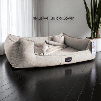 Beiges rechteckiges Haustierbett mit erhöhten Seiten, Kissen und dem Text "Inklusive Quick-Cover", auf dunklem Holzboden platziert.