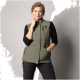 Ein Model trägt eine grüne ärmellose Weste mit einem Logo, kombiniert mit schwarzen Hosen, posierend vor einem grauen Hintergrund.