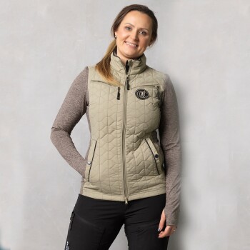 Eine Frau trägt eine hellgrüne gesteppte Weste über einem braunen Langarmshirt, kombiniert mit schwarzen Hosen, vor einem neutralen Hintergrund.