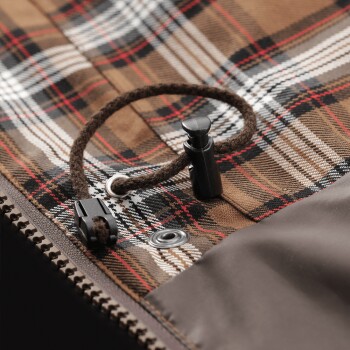 Nahaufnahme einer braunen karierten Haustierjacke mit Reißverschluss, Druckknopf und schwarzem Kordelstopper.