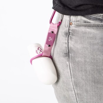 Eine Person in grauen Jeans hat eine weiße Haustier-Wasserflasche mit einem pinken Riemen und Karabiner an ihrer Taille befestigt.