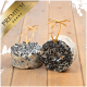 Zwei runde, hochwertige Vogelfutterkuchen mit einer Mischung aus schwarzen Samen und einer cremigen Basis, mit goldenen Bändern gebunden, auf einer Holzoberfläche.