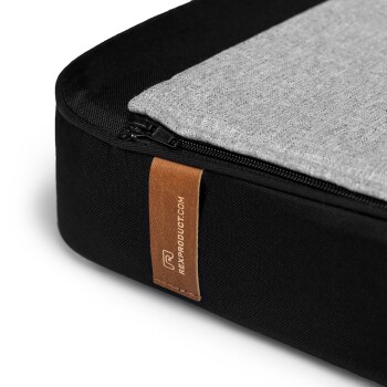 Nahaufnahme eines schwarzen Haustierbettes mit grauem Oberteil und Reißverschluss, mit einem Lederschild, auf dem "rexproduct.com" steht.