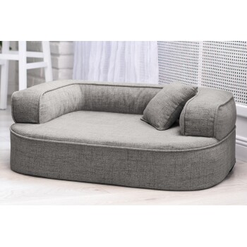 Graues Haustierbett mit gepolstertem Boden und erhöhten Seiten, mit einem kleinen Kissen, auf einem hellen Holzboden platziert.