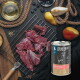 Dose LIEBESGUT-Hundefutter mit der Aufschrift 'Hirsch für Hunde' neben rohem Hirschfleisch auf einem Abkühlgitter mit Birnen, Beeren und Öl.