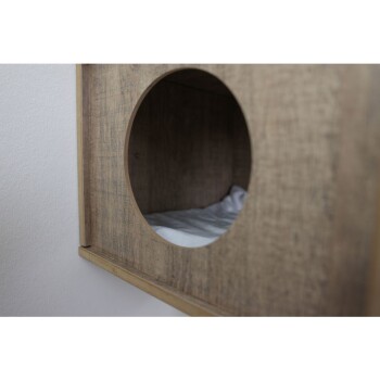 Drewniany domek dla zwierząt z okrągłym wejściem, z miękkim białym posłaniem w środku.