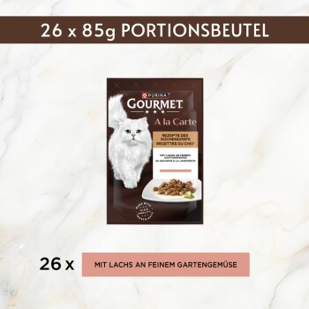 Purina Gourmet A la Carte Katzenfutter‑Beutel, weiße langhaarige Katze und Teller mit Futter; sichtbarer Text ‚26 x 85g PORTIONSBEUTEL‘