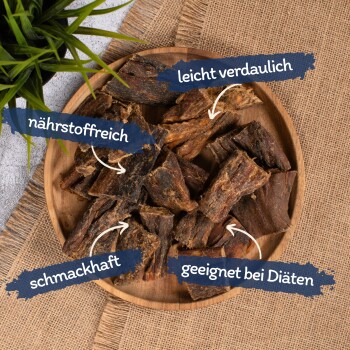 Eine Holzschale mit Tierleckerlis, beschriftet mit "nährstoffreich," "leicht verdaulich," "schmackhaft," und "geeignet bei Diäten," mit einer grünen Pflanze im Hintergrund.