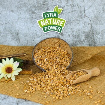 Eine Holzschüssel mit goldenen Körnern, die auf Jute fällt, mit einer Schaufel und einer Blume, und einem Etikett "LYRA NATURE POWER" darüber.