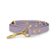 Eine lavendelfarbene Haustierleine mit goldenen Beschlägen und dekorativen Nieten, ordentlich auf einem weißen Hintergrund aufgerollt.