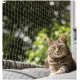 Eine entspannte getigerte Katze, die auf einem grauen Kissen liegt, mit einem grünen Außenhintergrund und einem Schutznetz im Vordergrund.