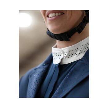 Nahaufnahme eines lächelnden Reiters in einer marineblauen Reitjacke mit funkelnden Details und einem weißen Kragen, unter einem Helm.