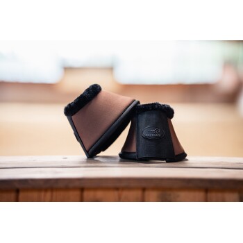 Zwei braune Pferdebeinschoner mit schwarzem Fleece-Futter und einem 'Equinate'-Logo, auf einer Holzoberfläche in einer sanft beleuchteten Innenumgebung platziert.