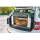 Großer brauner Hund ruht in einer grün-beigen, weichwandigen Transportbox mit orangefarbenen Seilgriffen im offenen Kofferraum eines weißen Autos