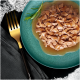 Gros plan d'une assiette turquoise remplie de nourriture humide pour chat finement hachée dans une sauce, garnie d'une branche de romarin, à côté d'une fourchette dorée.