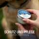 Eine Person hält eine Dose "Erste Hilfe Wundsalbe" für Haustiere, mit einem Hund im Hintergrund. Text: "Schutz und Pflege, Optimale Wundversorgung."