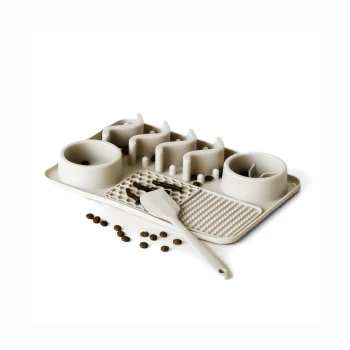 Futterstation für Haustiere mit zwei Schalen, einem Schaufel und einer strukturierten Matte, umgeben von verstreuten Haustierfutterpellets.