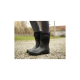 Schwarze Gummistiefel mit einem weichen Obermaterial, getragen von einer Person, die auf einer Kiesoberfläche steht, mit einem verschwommenen Außenhintergrund.