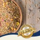 Eine Holzschüssel mit buntem Vogelfutter und einem goldenen Abzeichen mit der Aufschrift "Beste Qualität" und "10 Jahre" auf Deutsch.