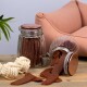 Ein Glasbehälter gefüllt mit Hundeleckerlis, einige fallen auf einen Holztisch, neben einem weißen Seilspielzeug und einer pinken Haustiercouch im Hintergrund.